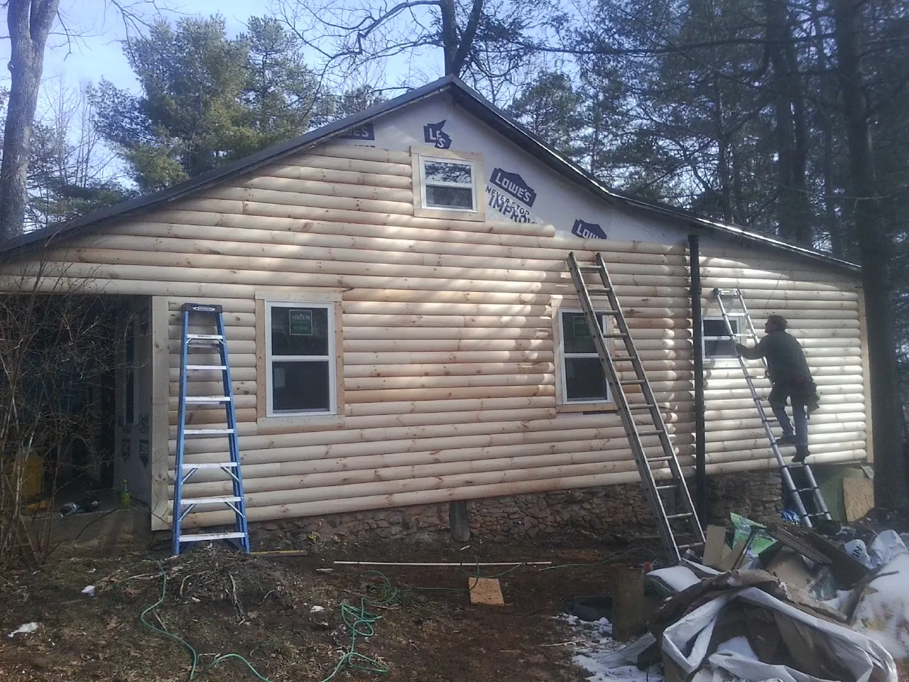 Ladders set against fresh log siding during an exterior remodel in Kenyon