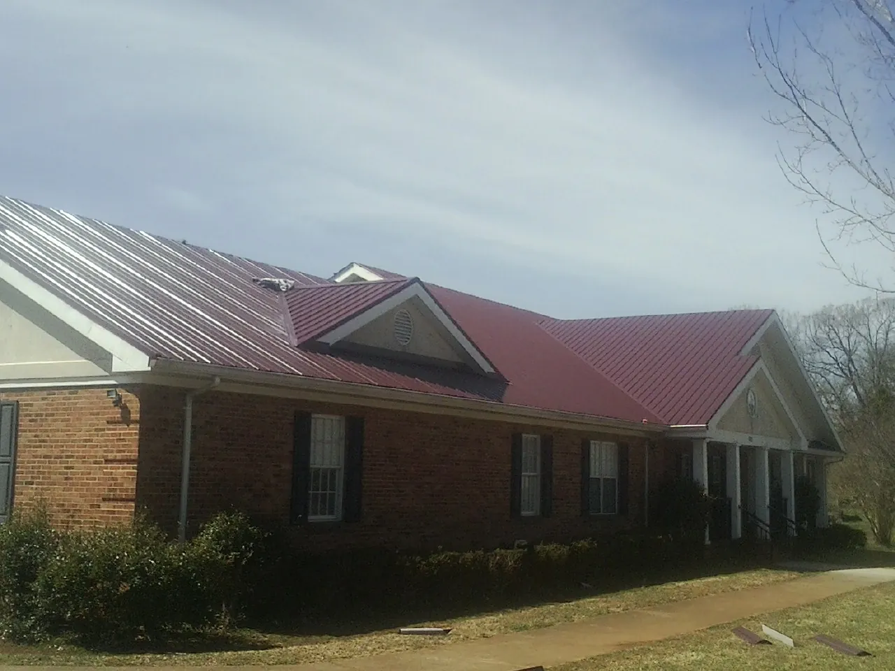 Red metal roof with gabled entries on a long brick building, from a Hail Damage Roof Repair job in Kenyon