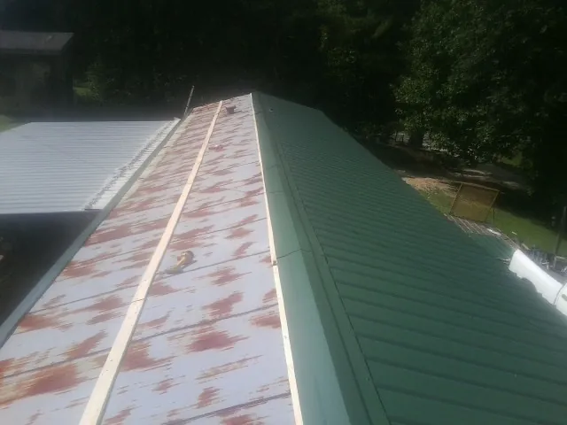 Old rusted panels beside newly installed green metal roofing — Wind Damage Roof Repair by Roofing Brothers in Kenyon