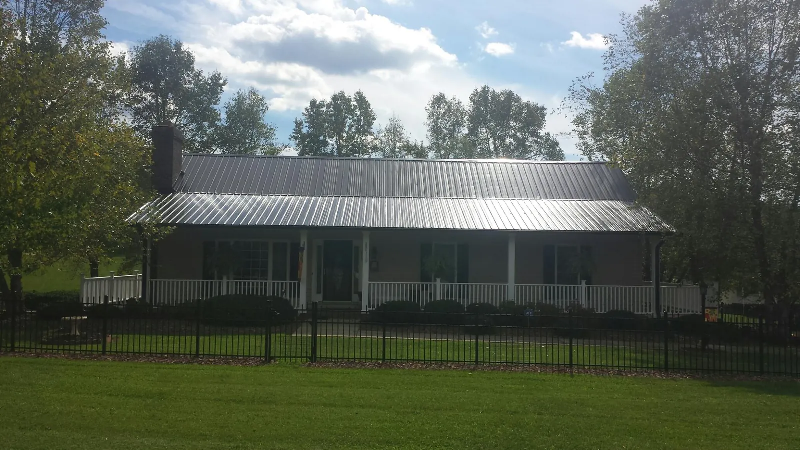 Gray metal roof on a brick ranch with a full width front porch — Gutter Guard Installation work by our crew in Kenyon